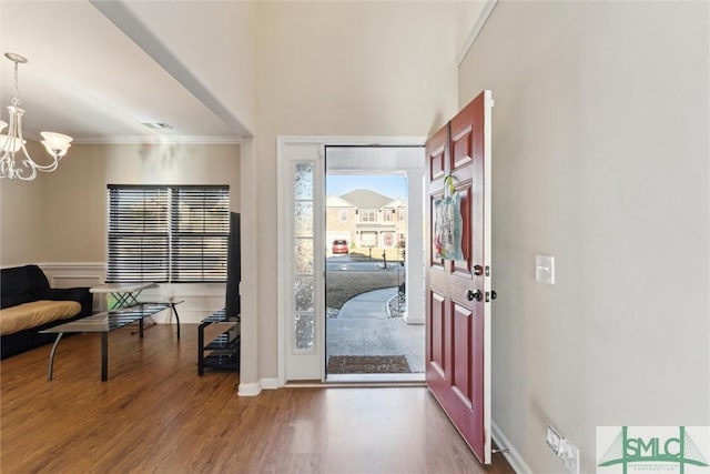 entryway with hardwood / wood-style flooring, ornamental molding, and an inviting chandelier