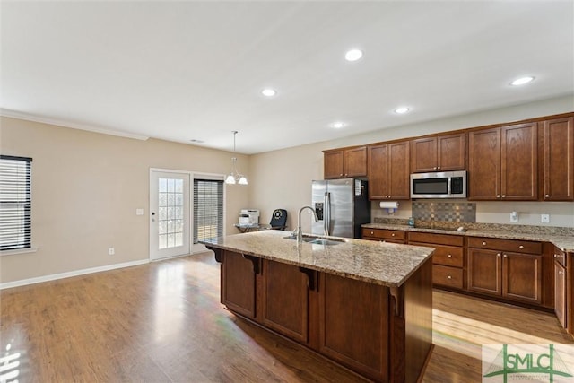 kitchen with appliances with stainless steel finishes, a kitchen breakfast bar, a kitchen island with sink, sink, and pendant lighting