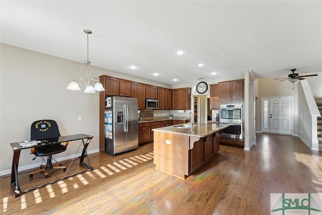 kitchen with ceiling fan with notable chandelier, hanging light fixtures, light stone countertops, a kitchen island, and stainless steel appliances