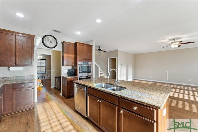 kitchen featuring light stone countertops, stainless steel appliances, a kitchen island with sink, sink, and light hardwood / wood-style flooring