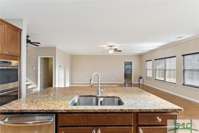 kitchen with light stone countertops, appliances with stainless steel finishes, ceiling fan, sink, and an island with sink