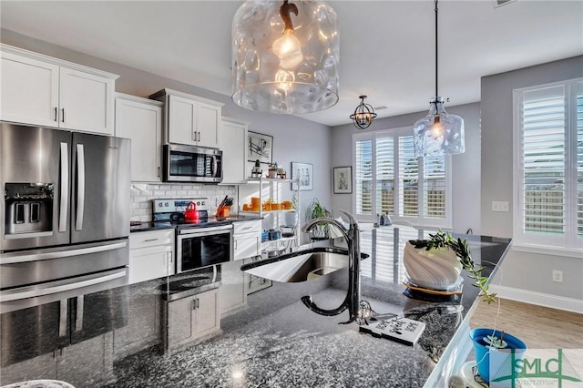 kitchen with white cabinetry, tasteful backsplash, dark stone counters, pendant lighting, and appliances with stainless steel finishes