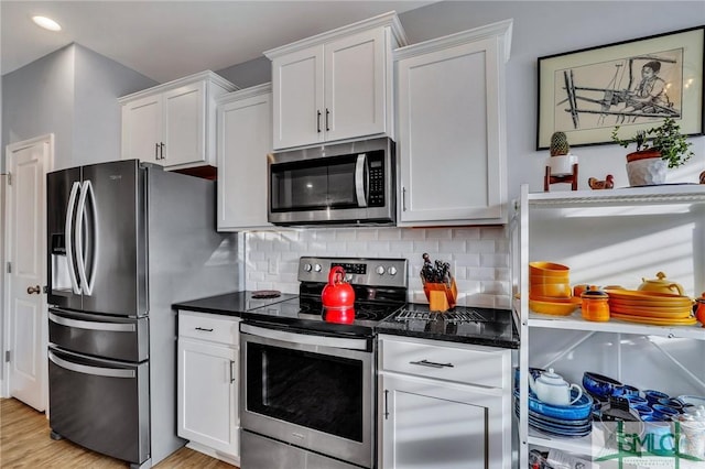 kitchen with white cabinets, decorative backsplash, dark stone countertops, light wood-type flooring, and stainless steel appliances