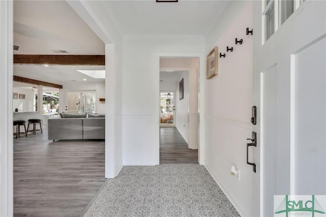 hallway featuring beamed ceiling, light wood-type flooring, and a healthy amount of sunlight