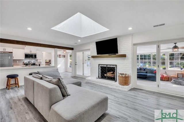 living room featuring a skylight, ceiling fan, a fireplace, and light hardwood / wood-style floors