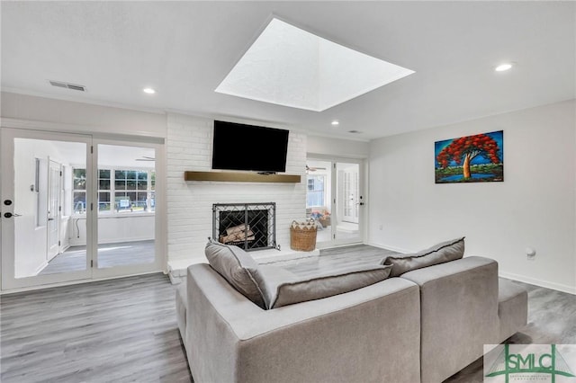 living room with a skylight, hardwood / wood-style floors, and a brick fireplace