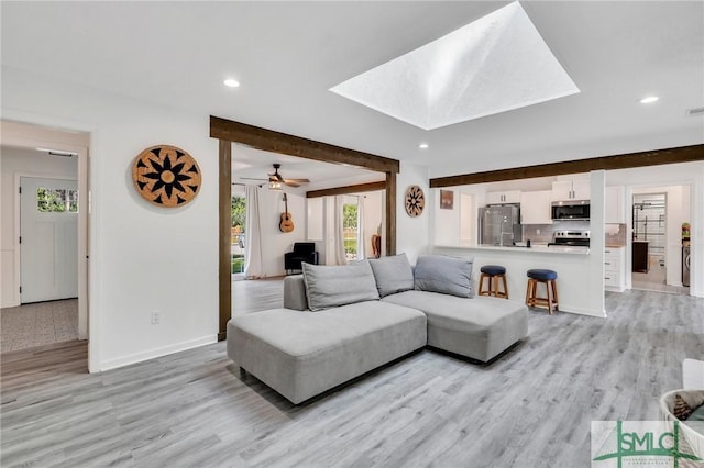 living room featuring beamed ceiling, light wood-type flooring, a skylight, and ceiling fan