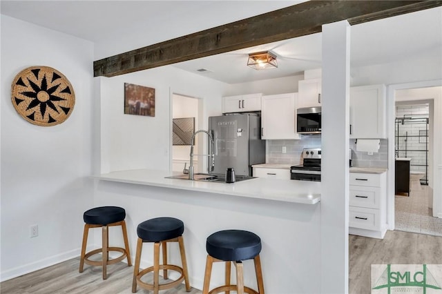 kitchen with appliances with stainless steel finishes, light wood-type flooring, tasteful backsplash, a breakfast bar, and white cabinetry