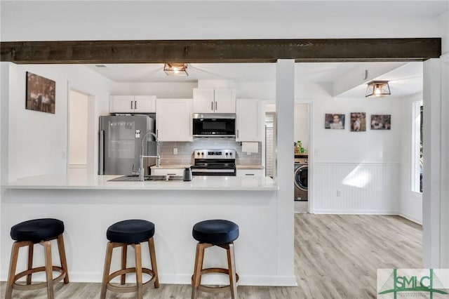 kitchen featuring white cabinetry, stainless steel appliances, a kitchen breakfast bar, washer / clothes dryer, and kitchen peninsula