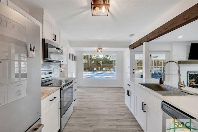 kitchen featuring sink, light wood-type flooring, appliances with stainless steel finishes, beam ceiling, and white cabinetry