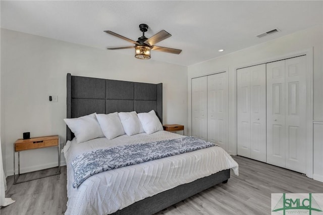 bedroom with light wood-type flooring, two closets, and ceiling fan