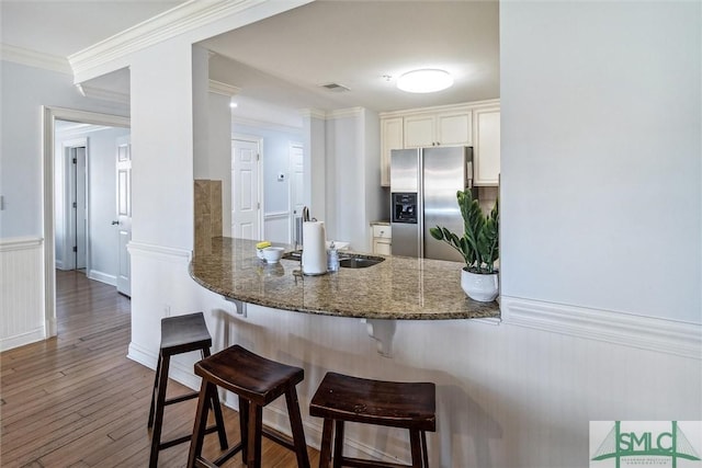 kitchen with a breakfast bar, dark wood-type flooring, dark stone counters, white cabinets, and stainless steel fridge