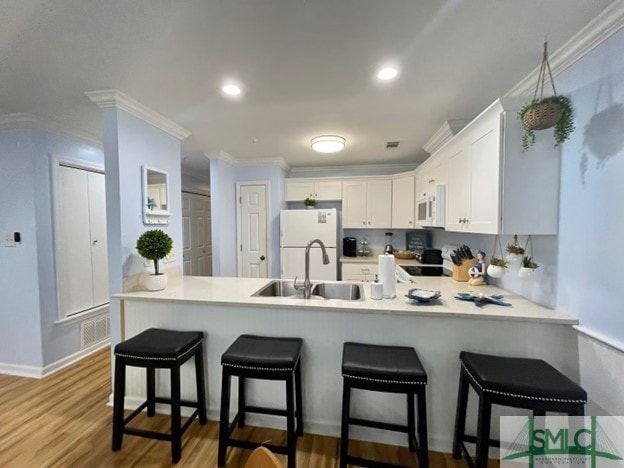 kitchen featuring kitchen peninsula, white appliances, sink, white cabinets, and a breakfast bar area