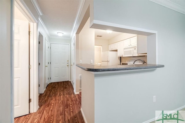 kitchen featuring kitchen peninsula, white appliances, crown molding, hardwood / wood-style floors, and white cabinetry