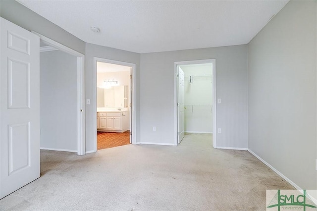 unfurnished bedroom with a walk in closet, light carpet, connected bathroom, and a closet