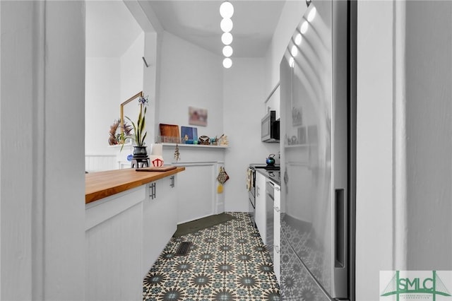 kitchen featuring stainless steel appliances, white cabinetry, and butcher block counters