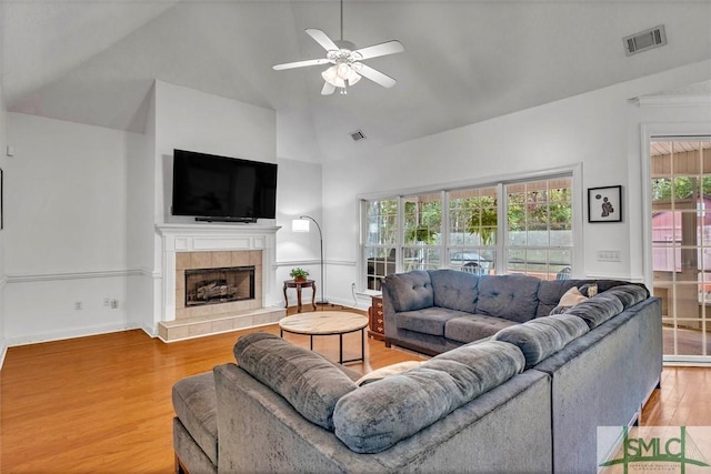 living room featuring hardwood / wood-style flooring, ceiling fan, high vaulted ceiling, and a tiled fireplace