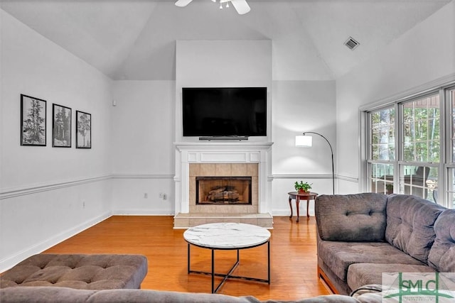 living room featuring a tiled fireplace, ceiling fan, wood-type flooring, and vaulted ceiling