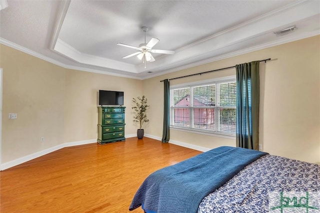 bedroom featuring hardwood / wood-style floors, a tray ceiling, ceiling fan, and crown molding