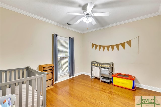 bedroom with ornamental molding, a textured ceiling, ceiling fan, a nursery area, and hardwood / wood-style floors