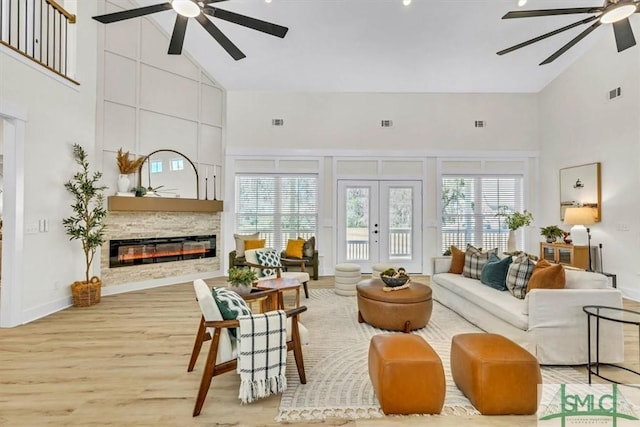 living room featuring light hardwood / wood-style floors, french doors, high vaulted ceiling, and a large fireplace