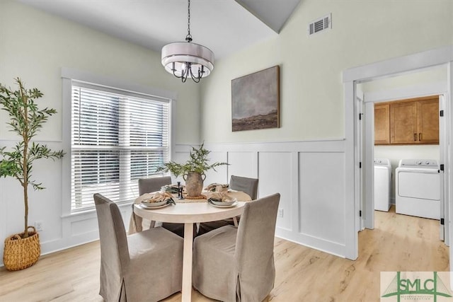 dining area featuring washer and dryer, lofted ceiling, a notable chandelier, and light hardwood / wood-style flooring