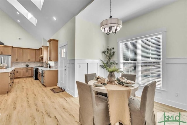 dining room with a skylight, light wood-type flooring, high vaulted ceiling, and plenty of natural light