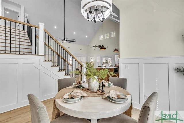 dining area with ceiling fan with notable chandelier, high vaulted ceiling, and light hardwood / wood-style floors