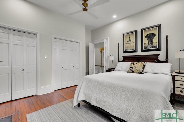 bedroom with hardwood / wood-style flooring, ceiling fan, and two closets