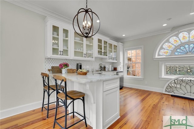 kitchen featuring white cabinets, an inviting chandelier, light stone countertops, and ornamental molding