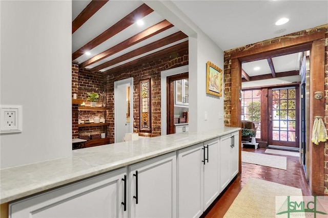 bar with light stone countertops, french doors, beamed ceiling, brick wall, and white cabinets