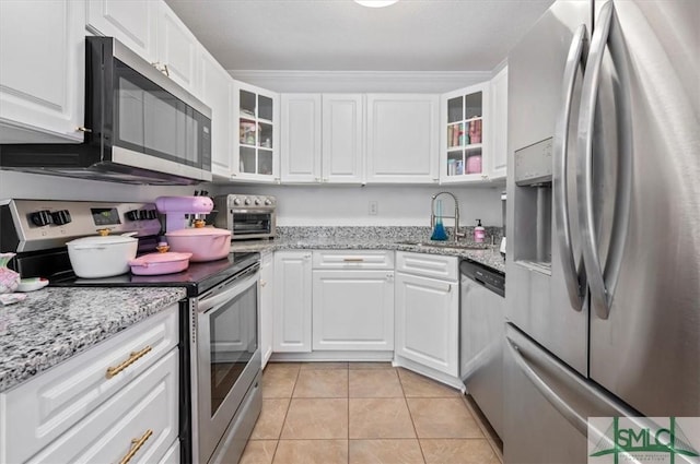 kitchen with appliances with stainless steel finishes, light tile patterned floors, white cabinetry, and light stone counters