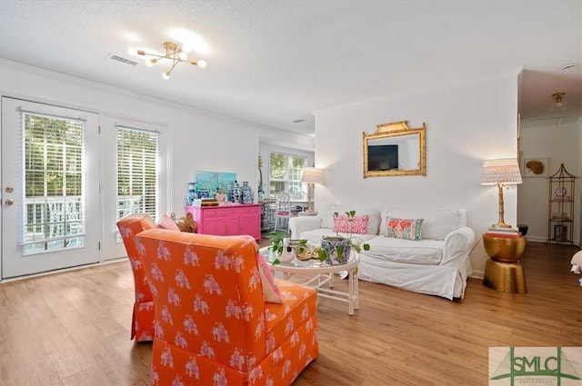 living room with a textured ceiling, light hardwood / wood-style floors, crown molding, and an inviting chandelier