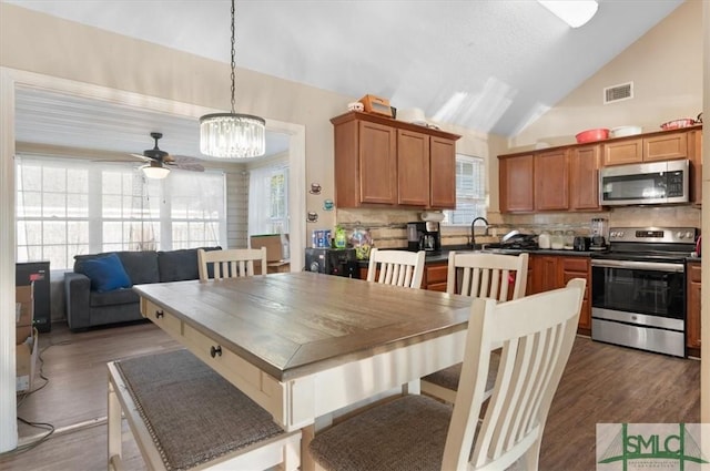 dining space with ceiling fan with notable chandelier, dark hardwood / wood-style floors, and high vaulted ceiling