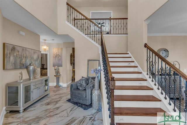 stairway featuring ornamental molding, a towering ceiling, and a notable chandelier