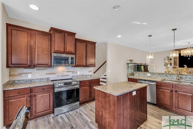 kitchen with appliances with stainless steel finishes, sink, light hardwood / wood-style flooring, backsplash, and pendant lighting