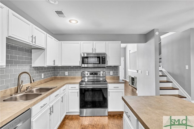 kitchen featuring sink, stainless steel appliances, light hardwood / wood-style floors, decorative backsplash, and white cabinets