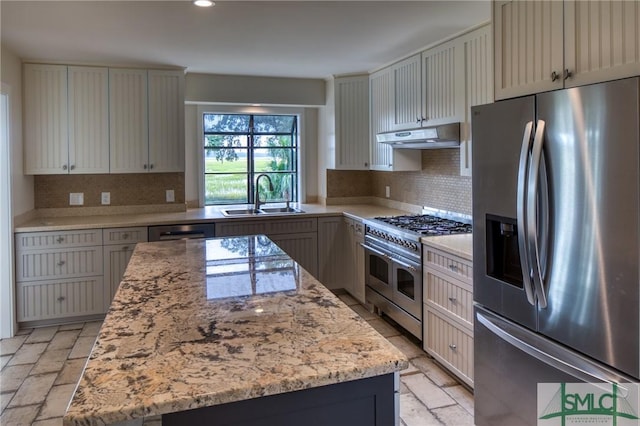 kitchen featuring under cabinet range hood, a kitchen island, a sink, appliances with stainless steel finishes, and light stone countertops