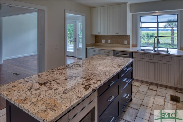 kitchen with light stone counters, a sink, visible vents, a center island, and tasteful backsplash