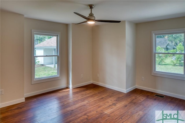 unfurnished room with a ceiling fan, wood-type flooring, visible vents, and baseboards