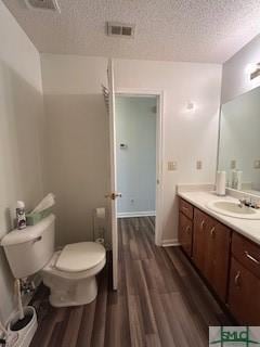 bathroom with hardwood / wood-style flooring, vanity, toilet, and a textured ceiling