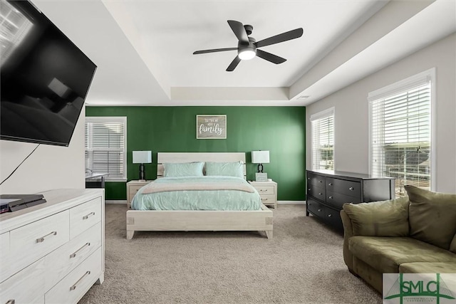 bedroom with ceiling fan, light carpet, and a tray ceiling