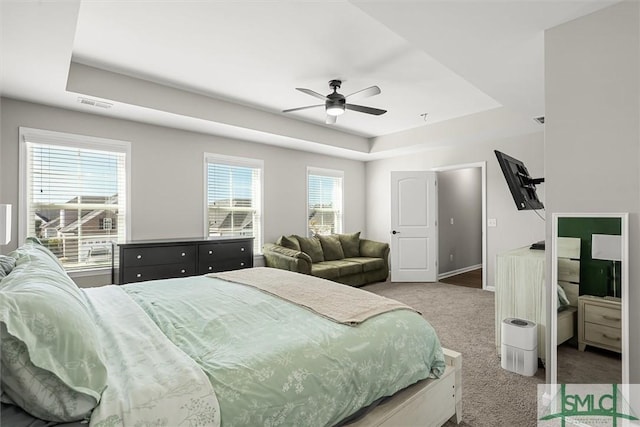 bedroom featuring a raised ceiling, multiple windows, and ceiling fan