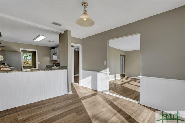 kitchen with light stone countertops, white cabinetry, stainless steel fridge, light hardwood / wood-style floors, and decorative light fixtures