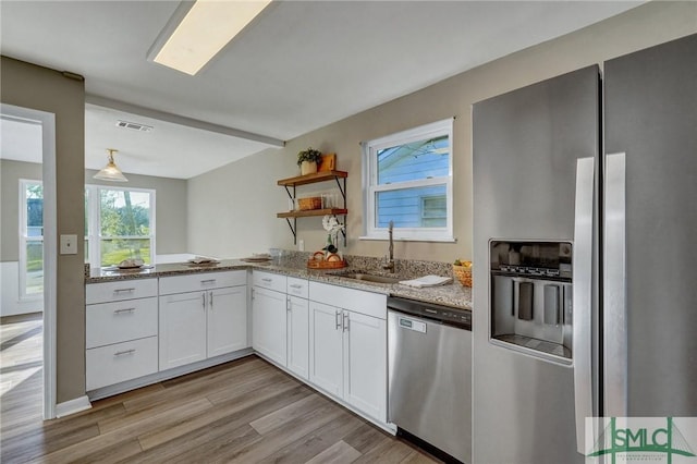 kitchen featuring sink, light wood-type flooring, appliances with stainless steel finishes, light stone counters, and white cabinetry