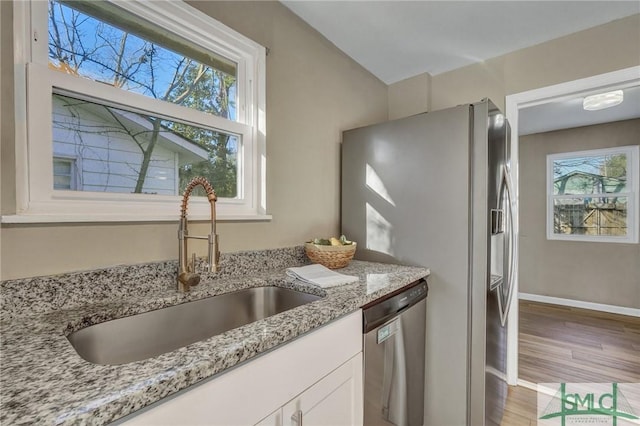 kitchen with wood-type flooring, sink, light stone countertops, appliances with stainless steel finishes, and white cabinetry