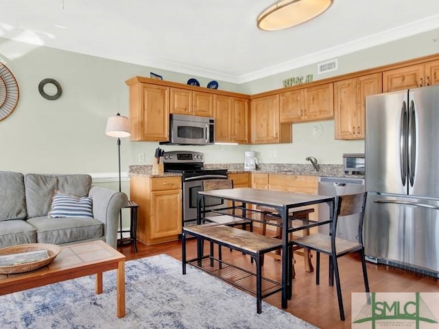 kitchen featuring appliances with stainless steel finishes, dark hardwood / wood-style floors, light stone counters, and ornamental molding