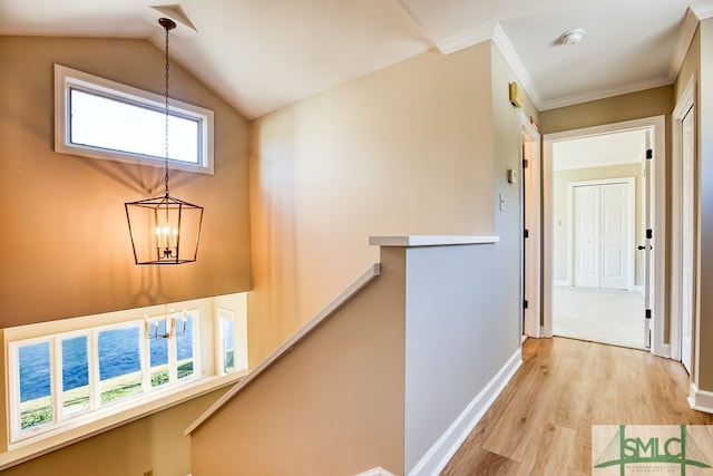 hallway featuring lofted ceiling, light wood-style flooring, an upstairs landing, baseboards, and ornamental molding