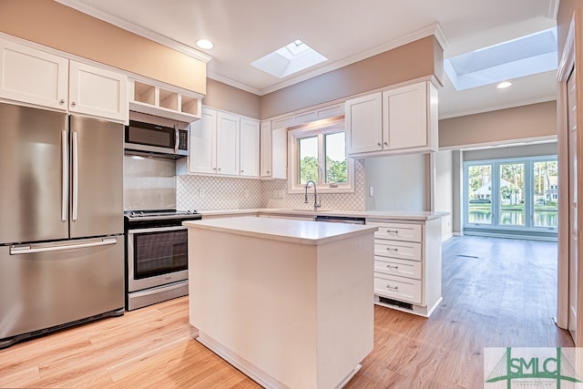 kitchen featuring stainless steel appliances, a skylight, a kitchen island, white cabinets, and ornamental molding