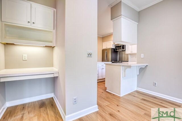 kitchen featuring a kitchen breakfast bar, crown molding, decorative backsplash, white cabinets, and appliances with stainless steel finishes